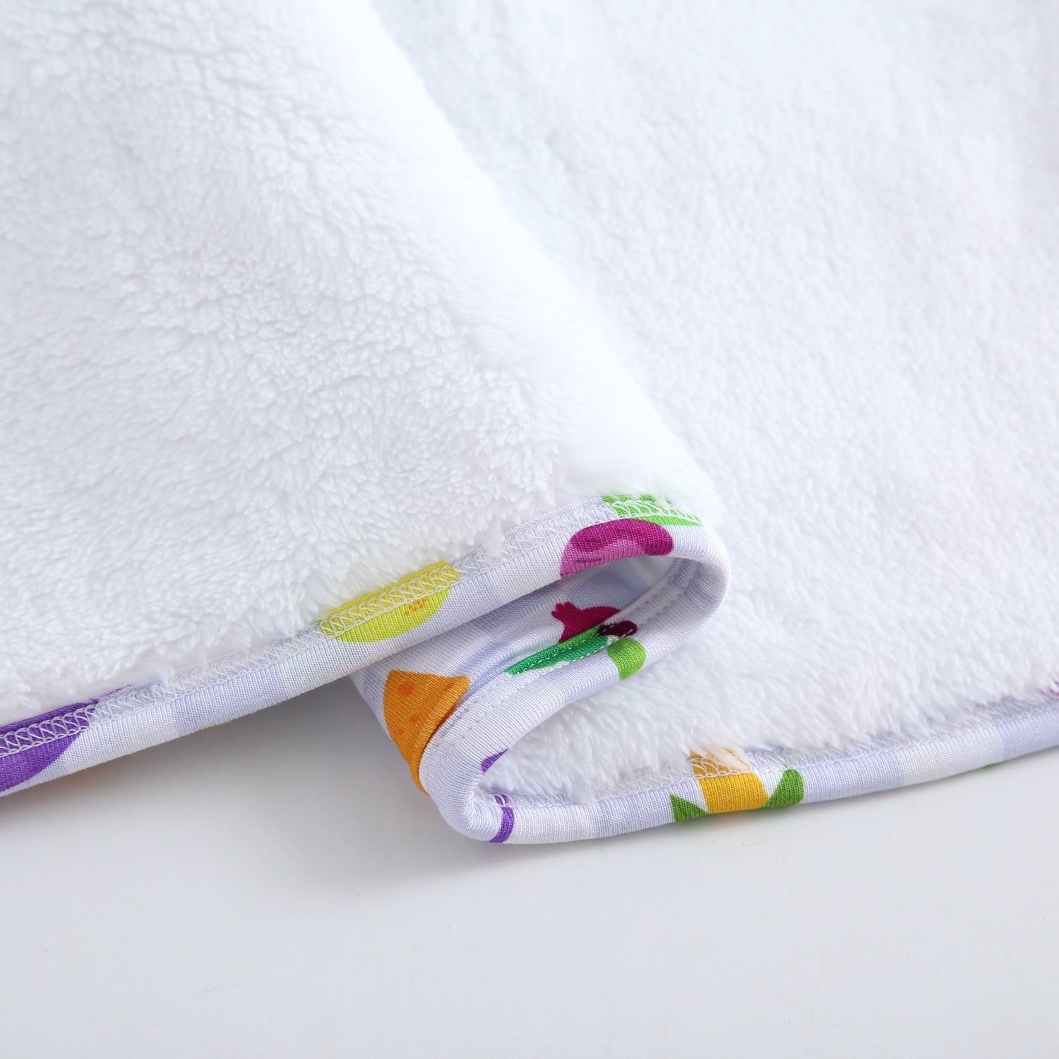A white plush blanket with a colorful patterned trim.