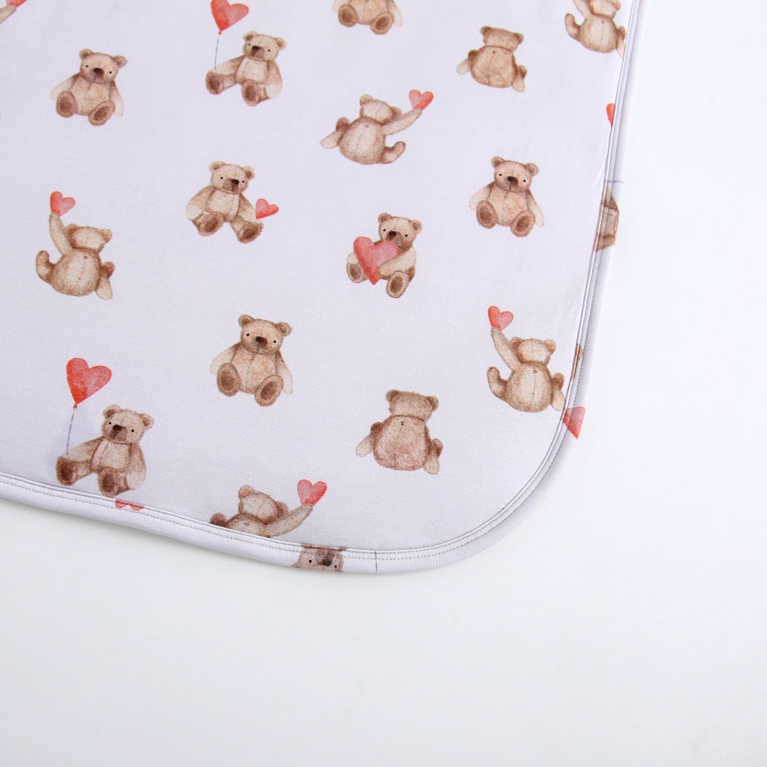 A light gray blanket with a pattern of watercolor teddy bears holding red hearts.
