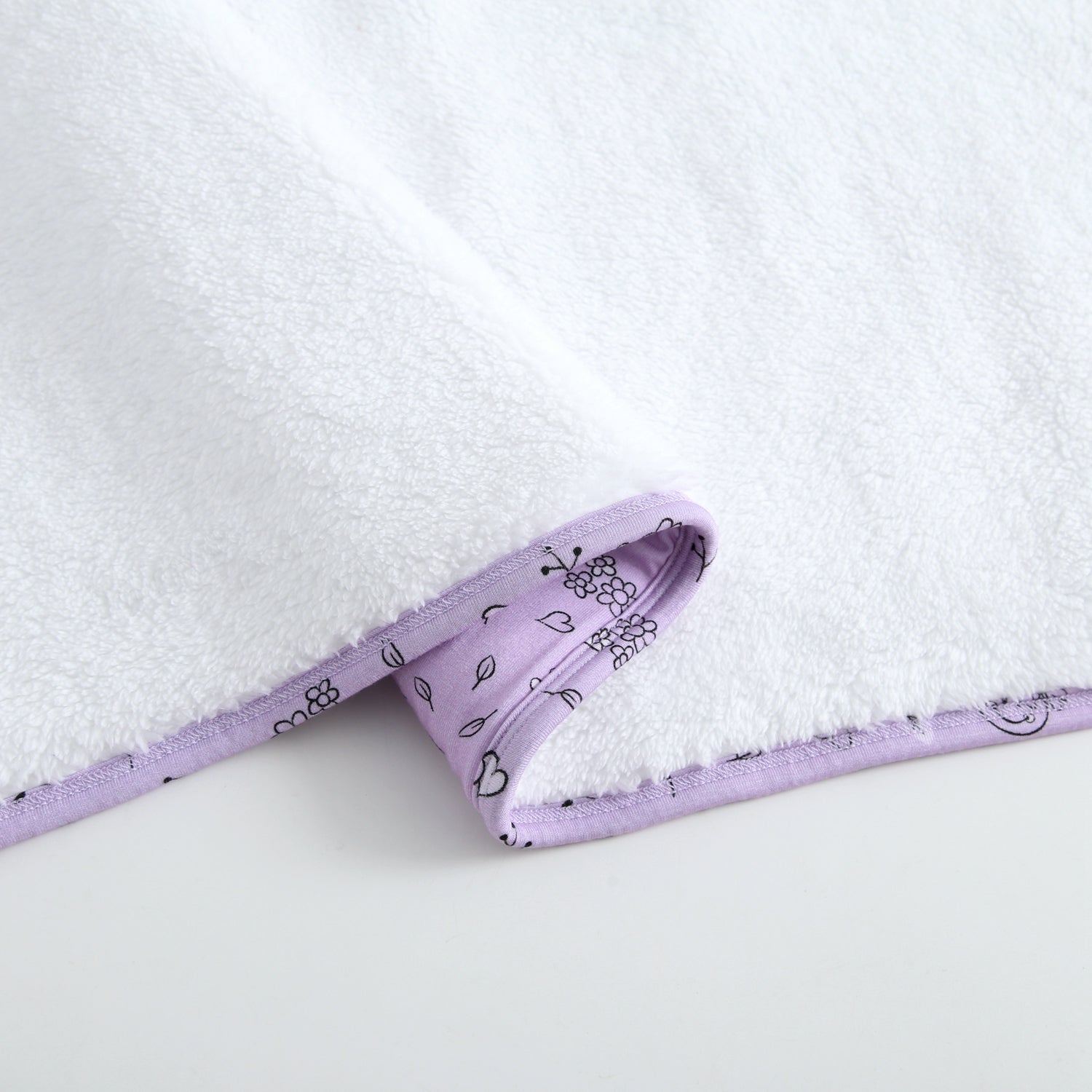 A white plush blanket with a lilac trim featuring a doodle print.