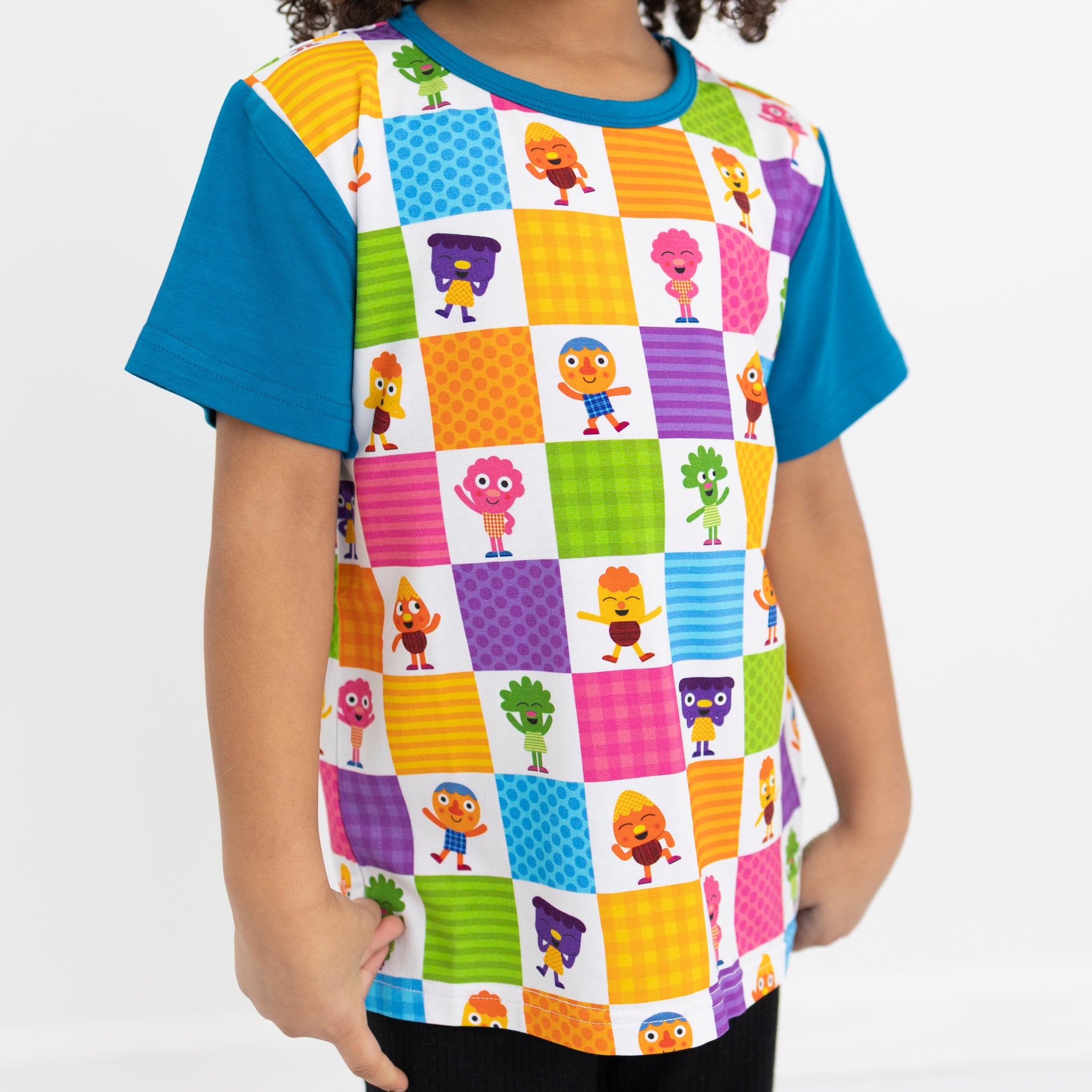 A child wears a colorful Noodle & Pals checkered T-shirt with blue sleeves and a crew neck.