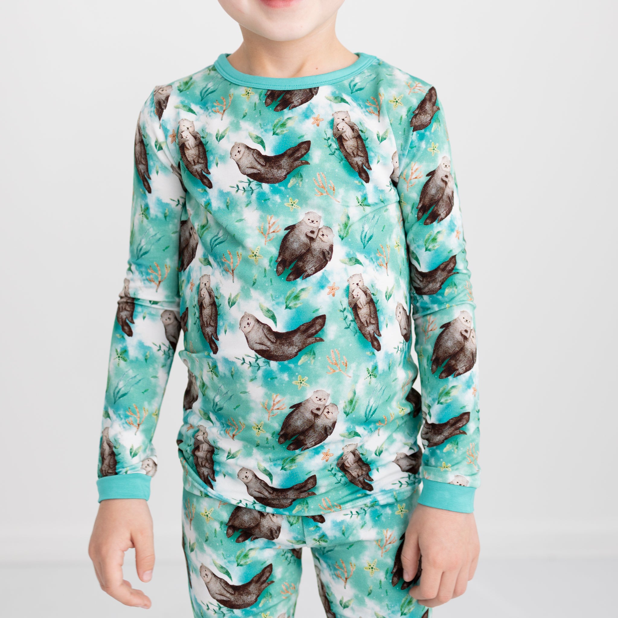 A child wears a long-sleeved bamboo pajama set featuring a watercolor otter and kelp print.