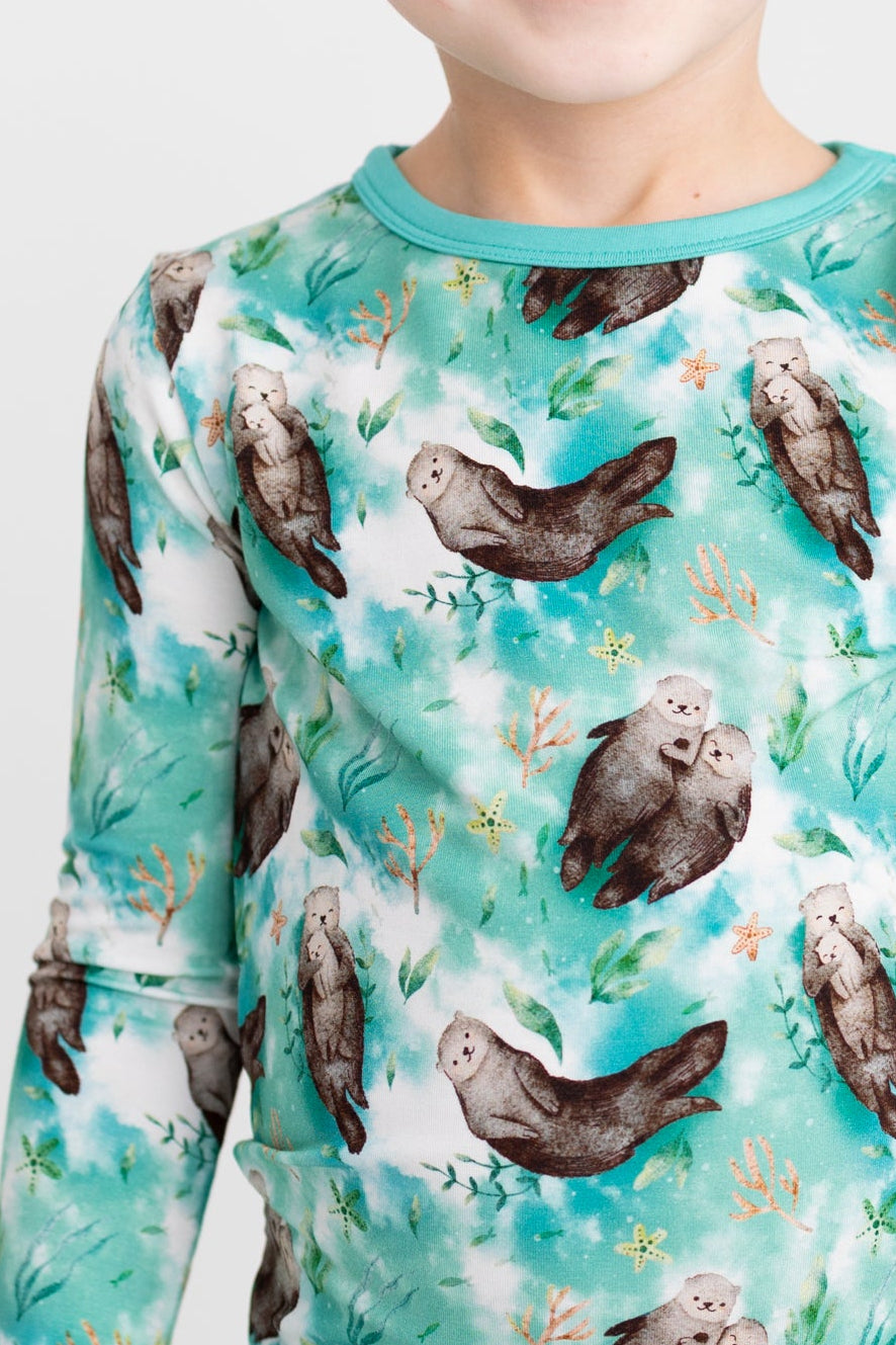 A child wears a long-sleeved pajama set with a repeating pattern of otters and sea plants.
