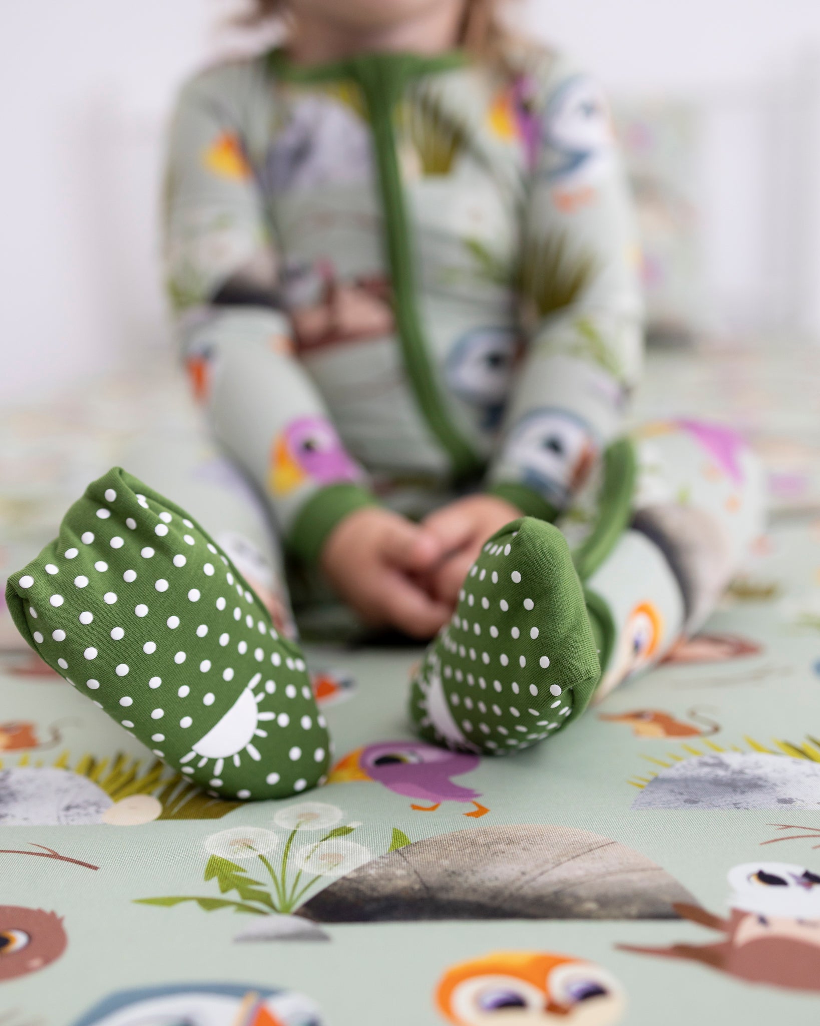 Green footed pajamas with white polka dots and Puffin Rock characters.