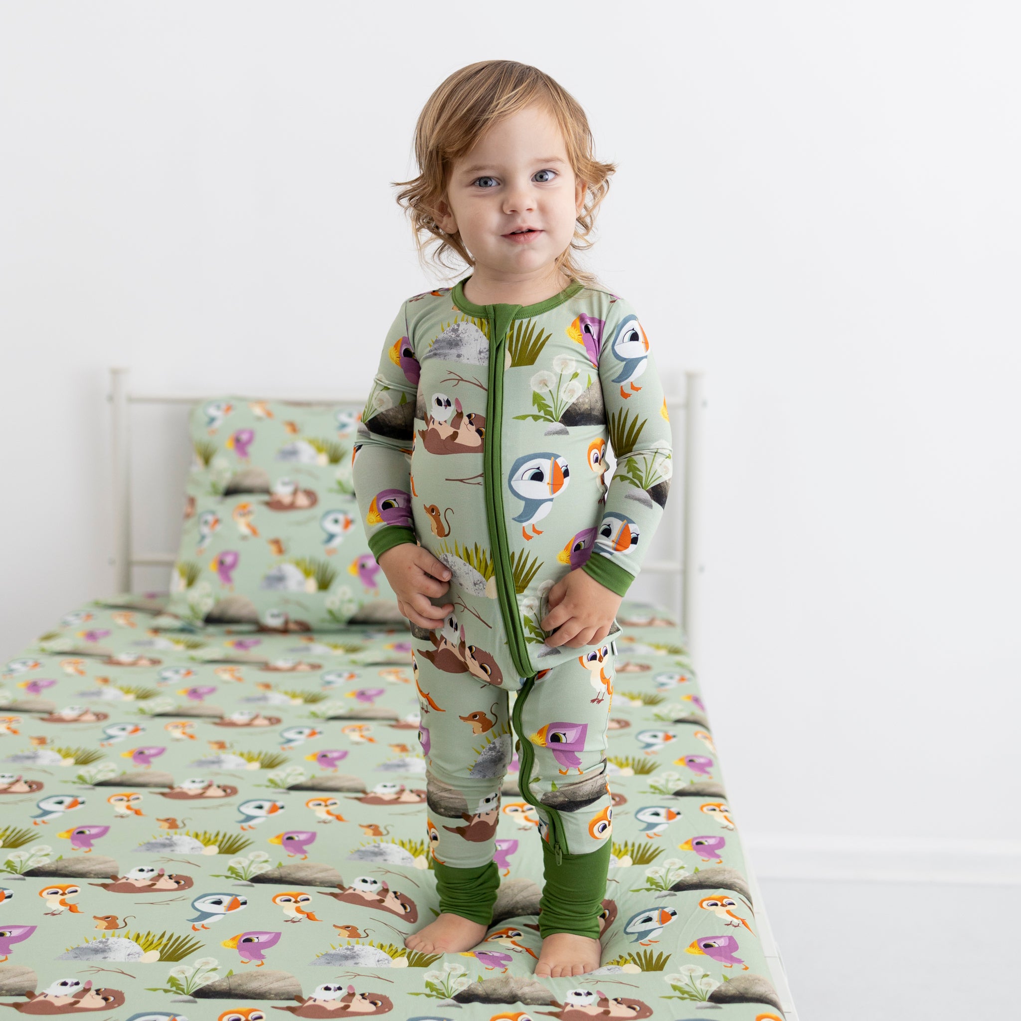 A toddler stands on a bed with a Tencel modal sheet and pillowcase featuring a Puffin Rock print.