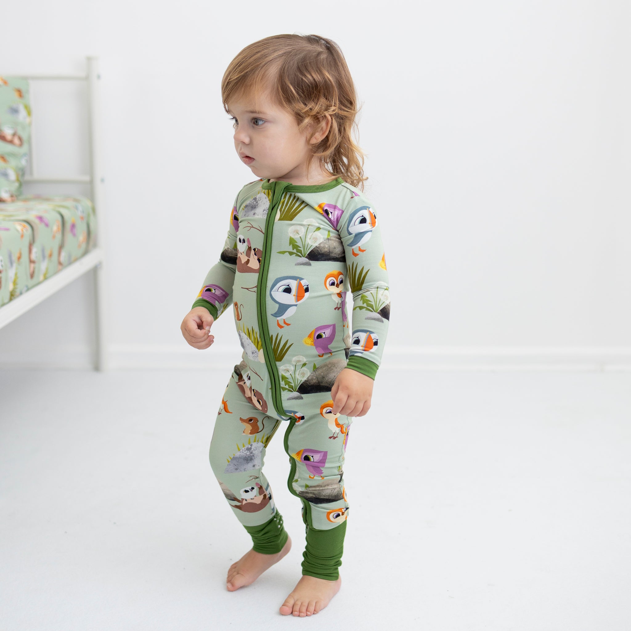 A toddler wears a light green pajama set with a Puffin Rock print.
