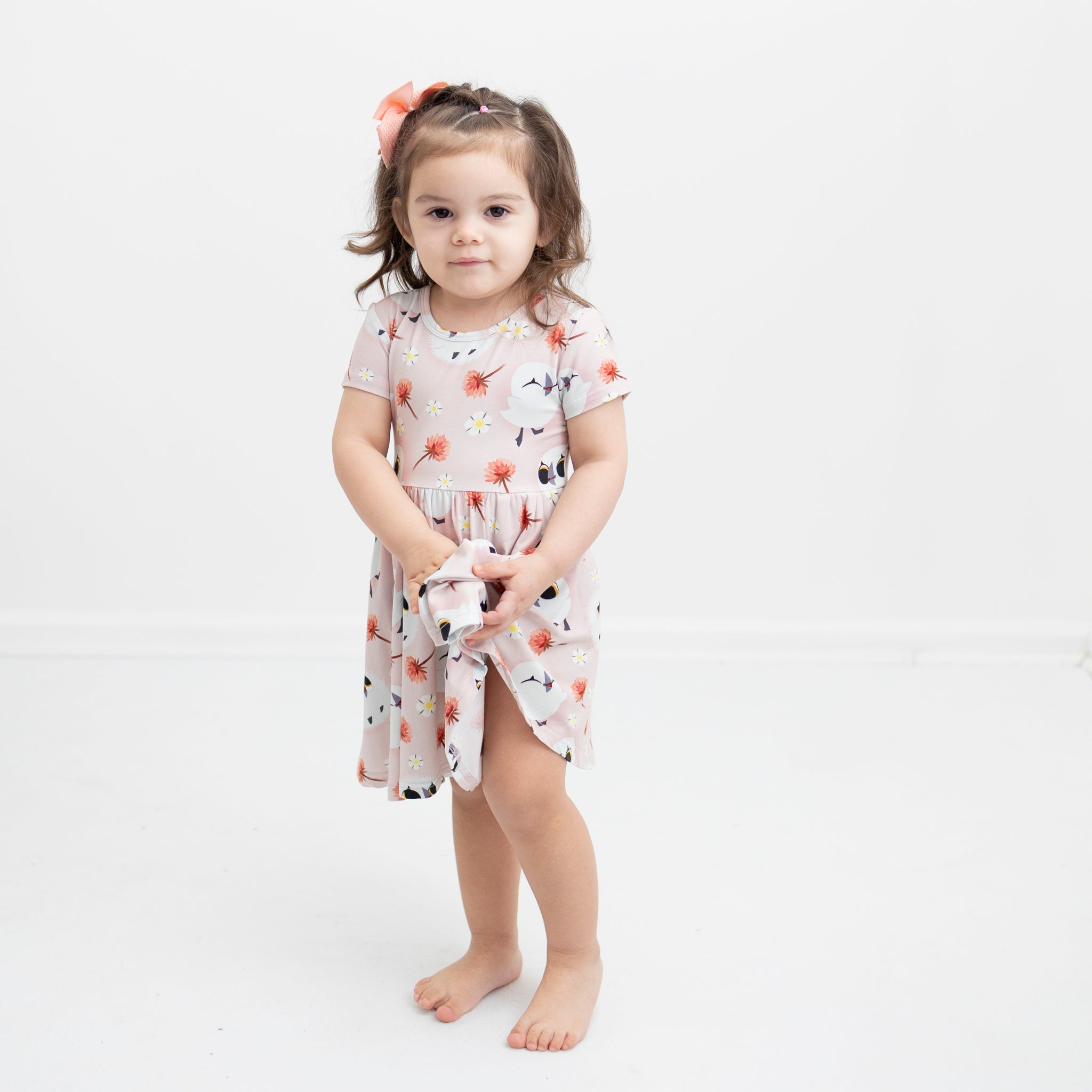 A young girl in a pink dress with a puffin print and a peach bow.