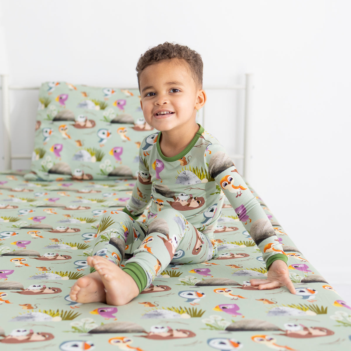 A young boy sits on a bed with Puffin Rock™ themed bedding.