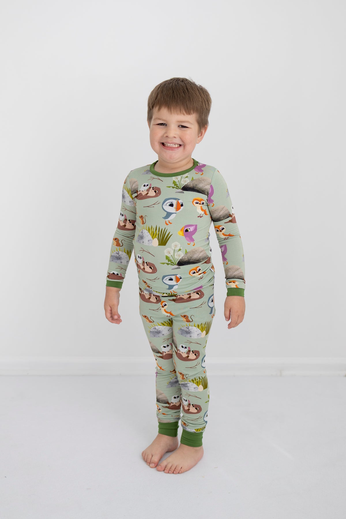 A young boy smiles in a light green pajama set with a Puffin Rock print.