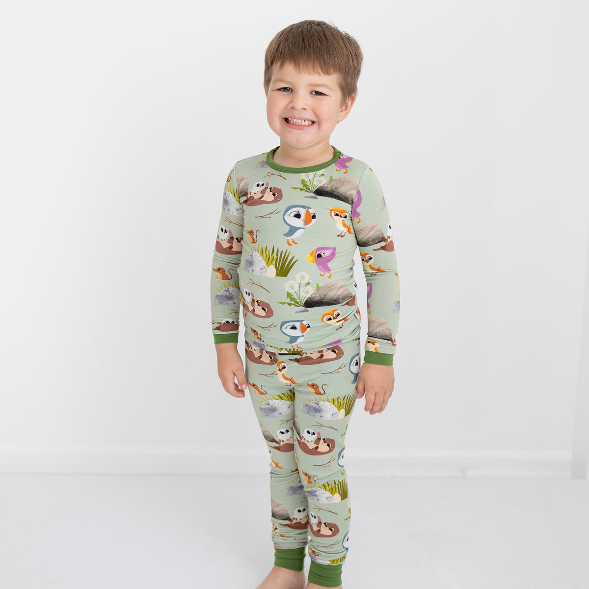 A young boy smiles in a light green pajama set with a Puffin Rock™ print.