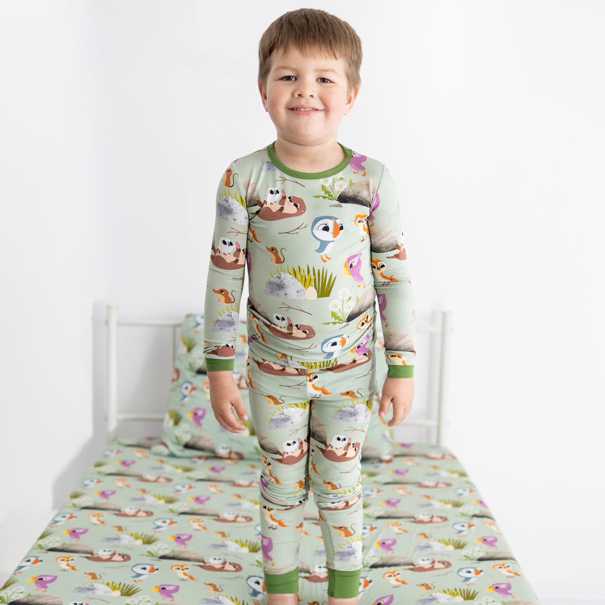 A young boy stands in a light green pajama set with a Puffin Rock print.