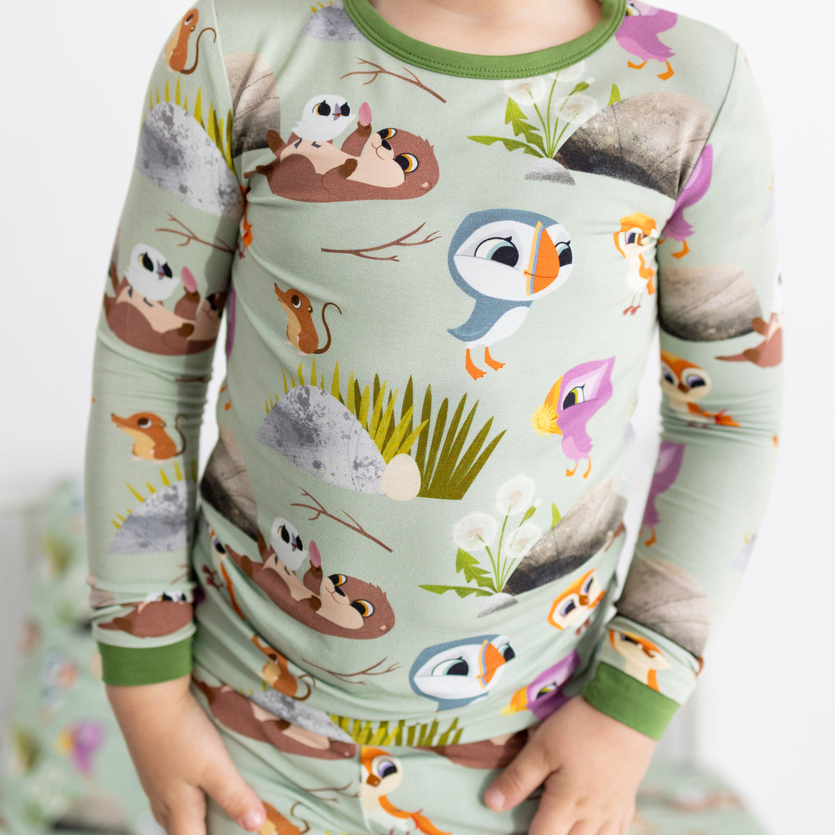 A child wears light green pajamas with a Puffin Rock™ print featuring puffins, otters, and other woodland creatures.