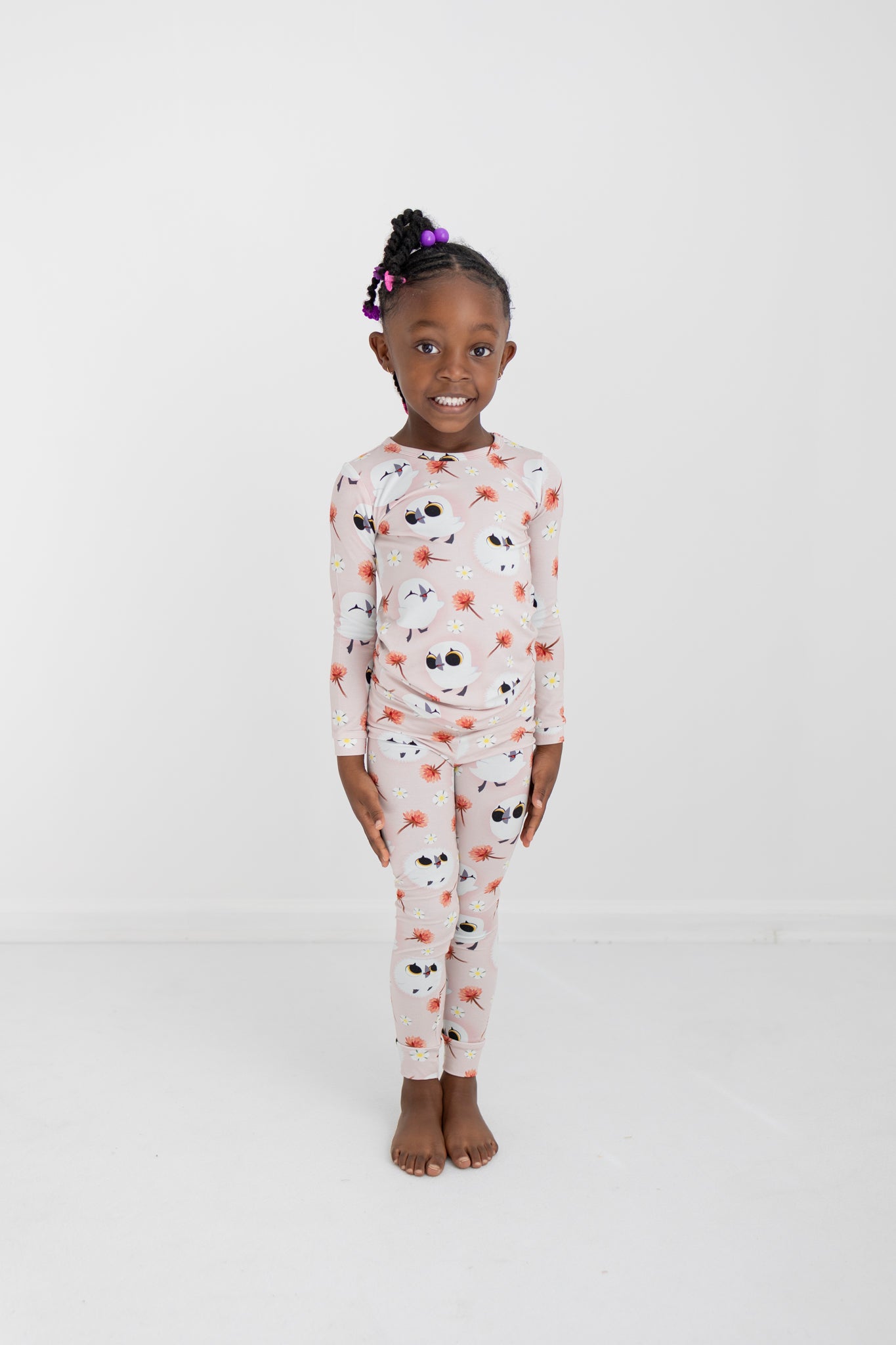 A young Black girl smiles in a pink pajama set with a puffin print.