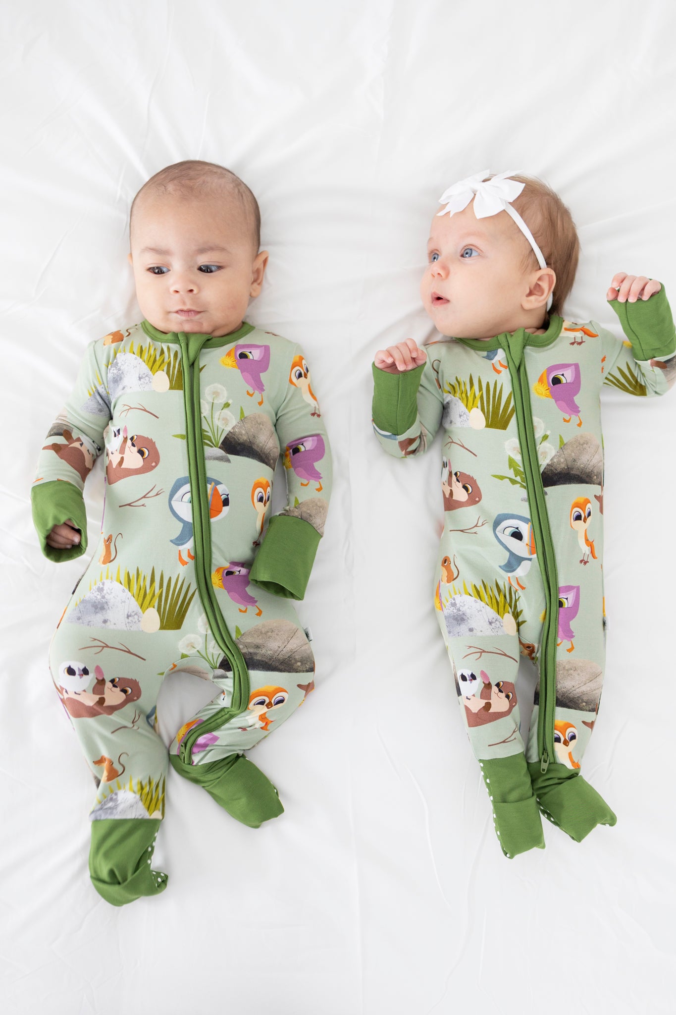 Two babies in light green pajamas with a Puffin Rock print.
