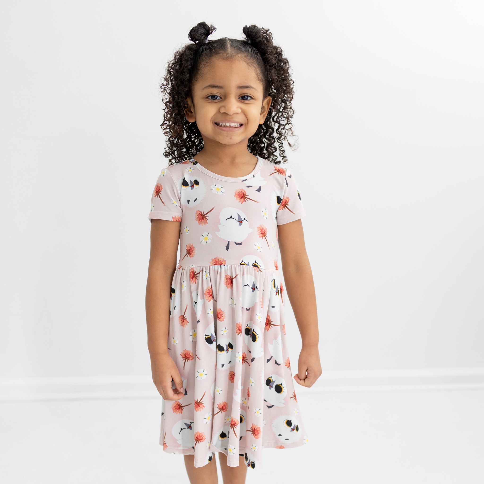 A young girl smiles in a pink dress with a puffin and floral print.