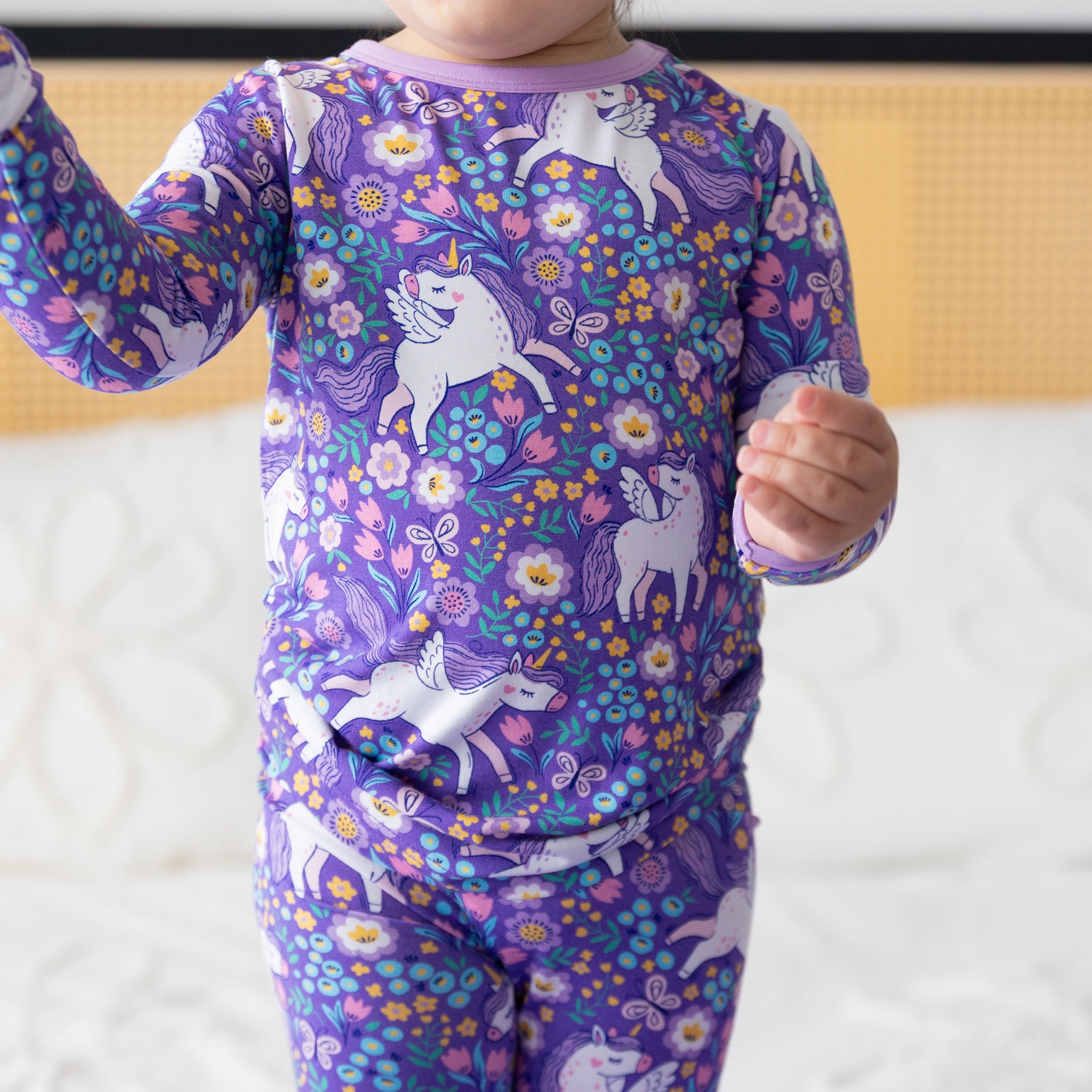 A toddler wears a purple long-sleeve pajama set featuring a unicorn and floral print.