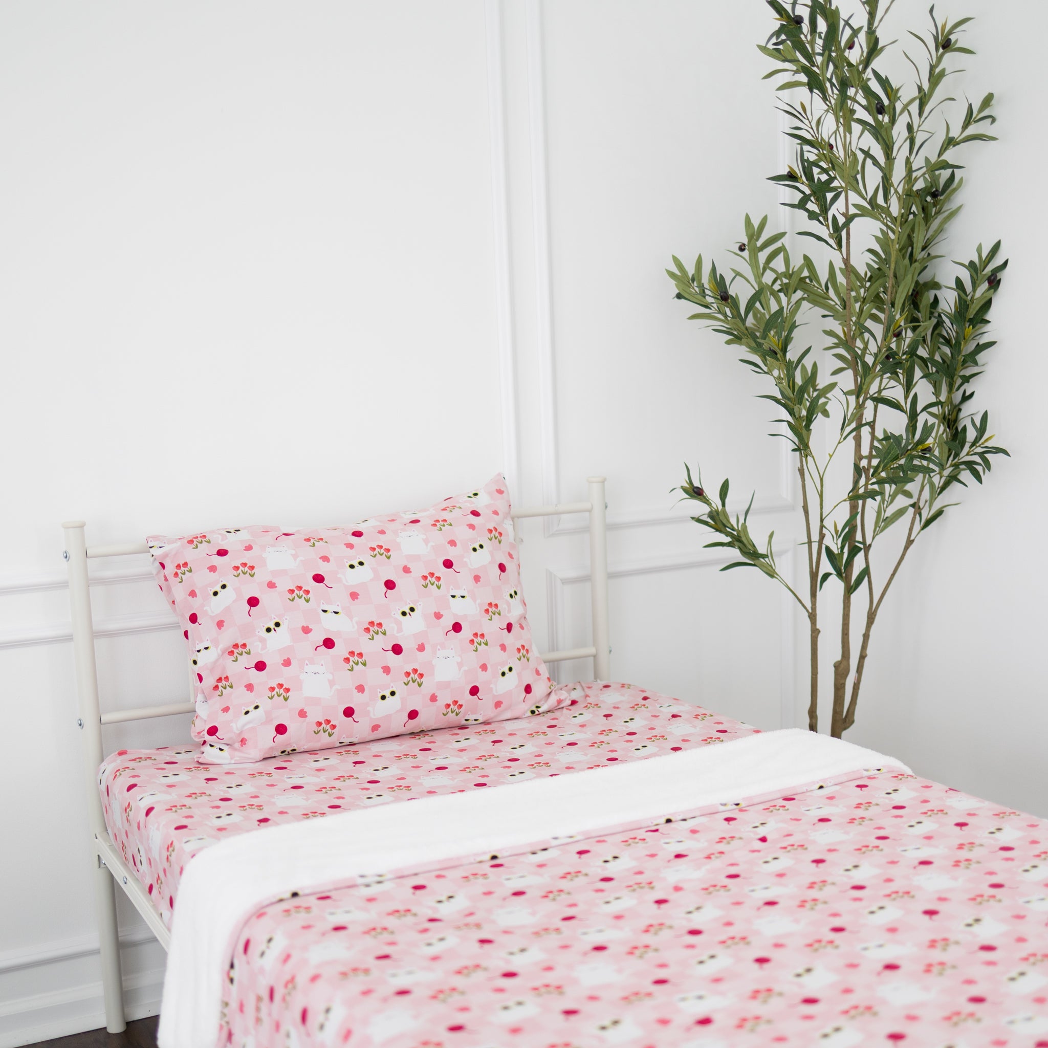 A twin bed with a white metal frame is dressed in pink bedding featuring a cat and floral pattern.