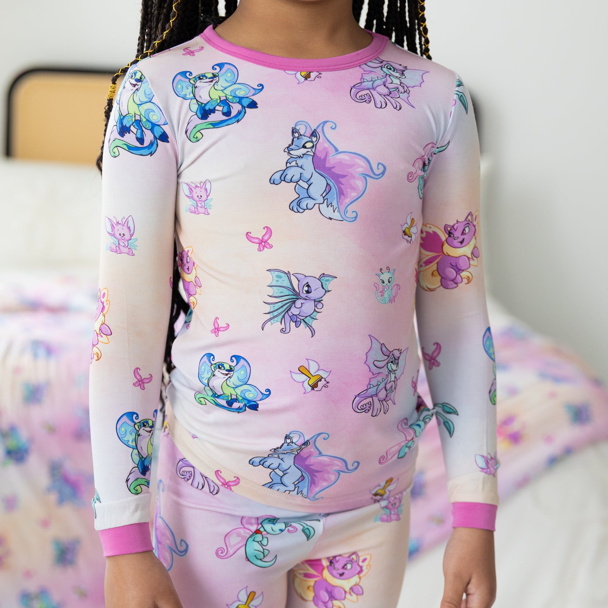 A child wears a long-sleeve pajama set featuring a colorful Neopets Faerie print on a pink gradient.