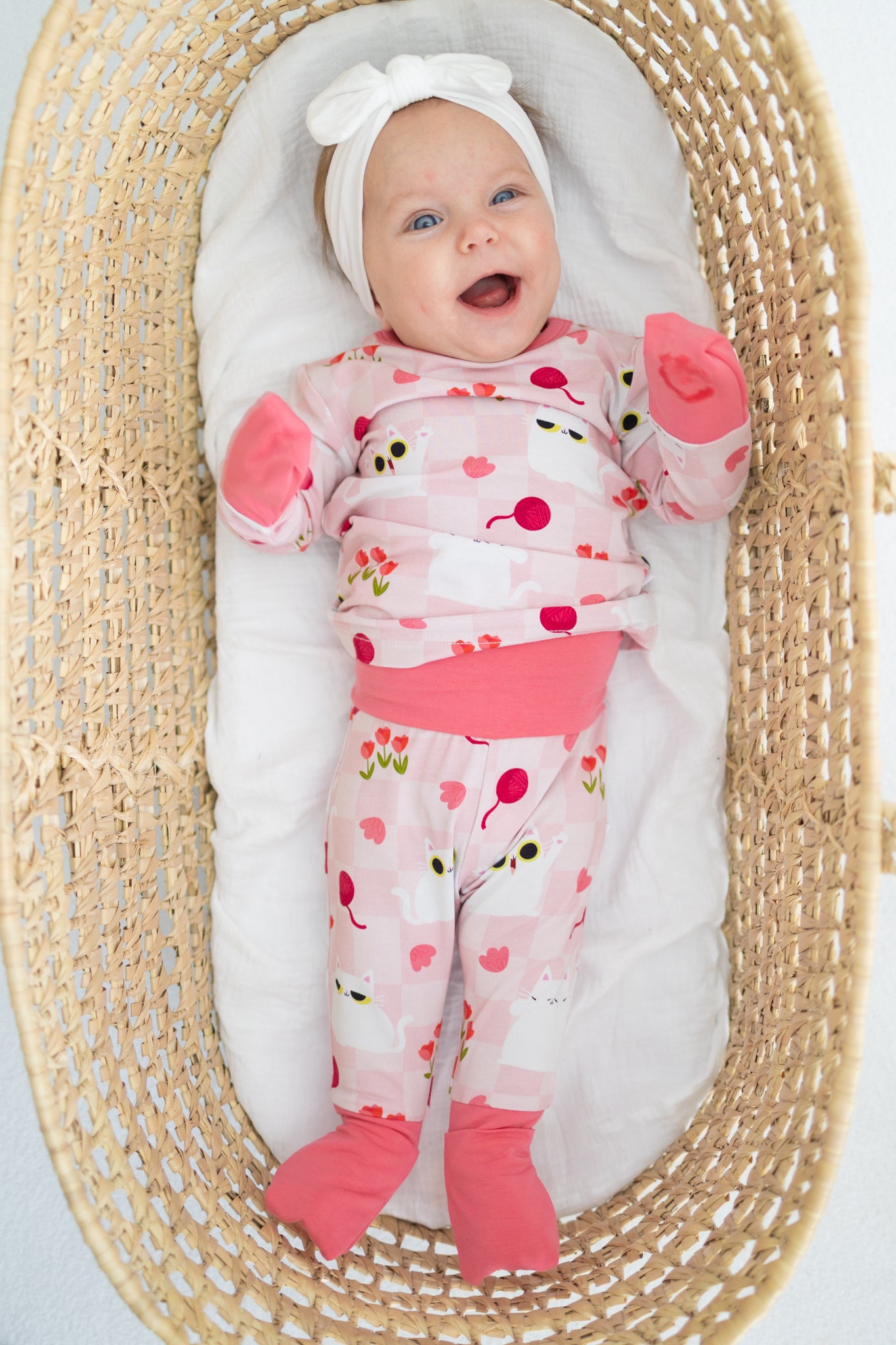 A baby wearing a pink and white cat-patterned pajama set with a matching bow headband.