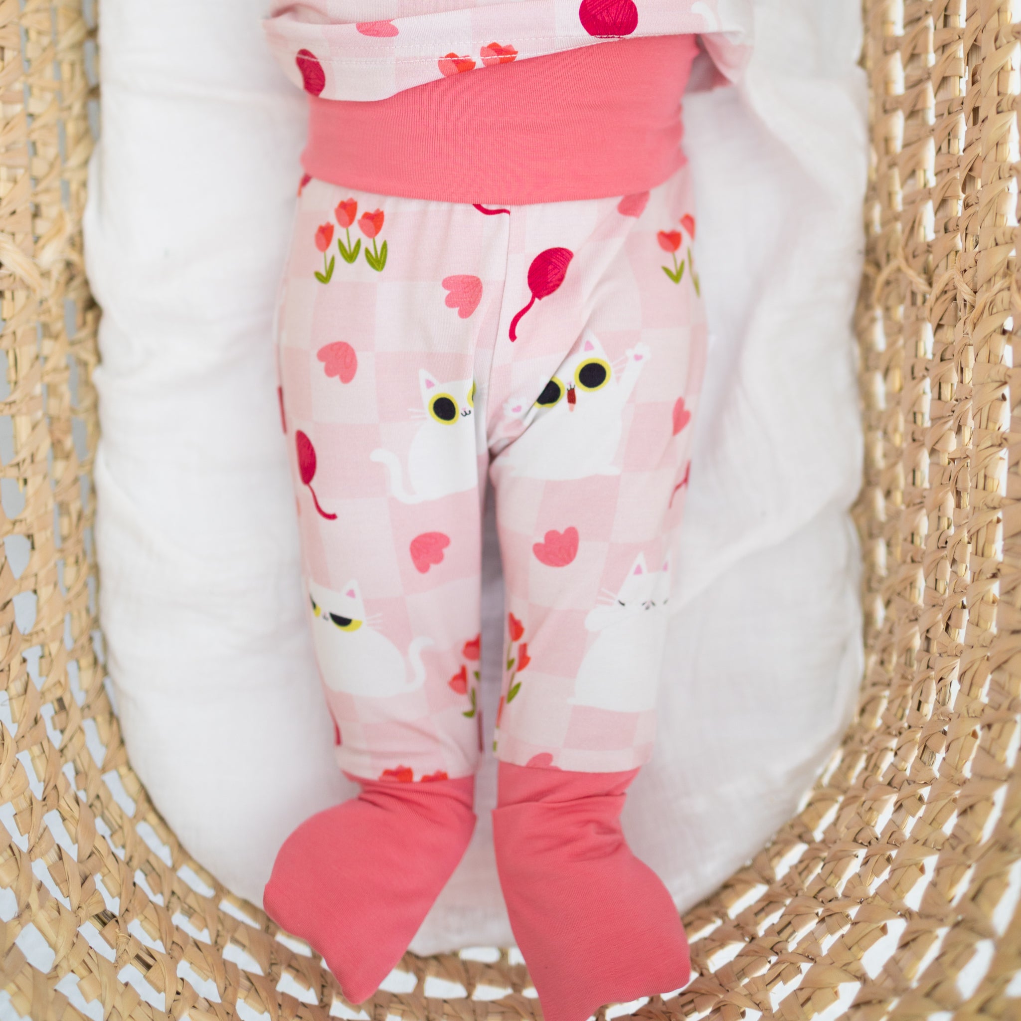 A baby wearing pink Tencel Modal pajamas featuring a white cat, balloon, and tulip print.