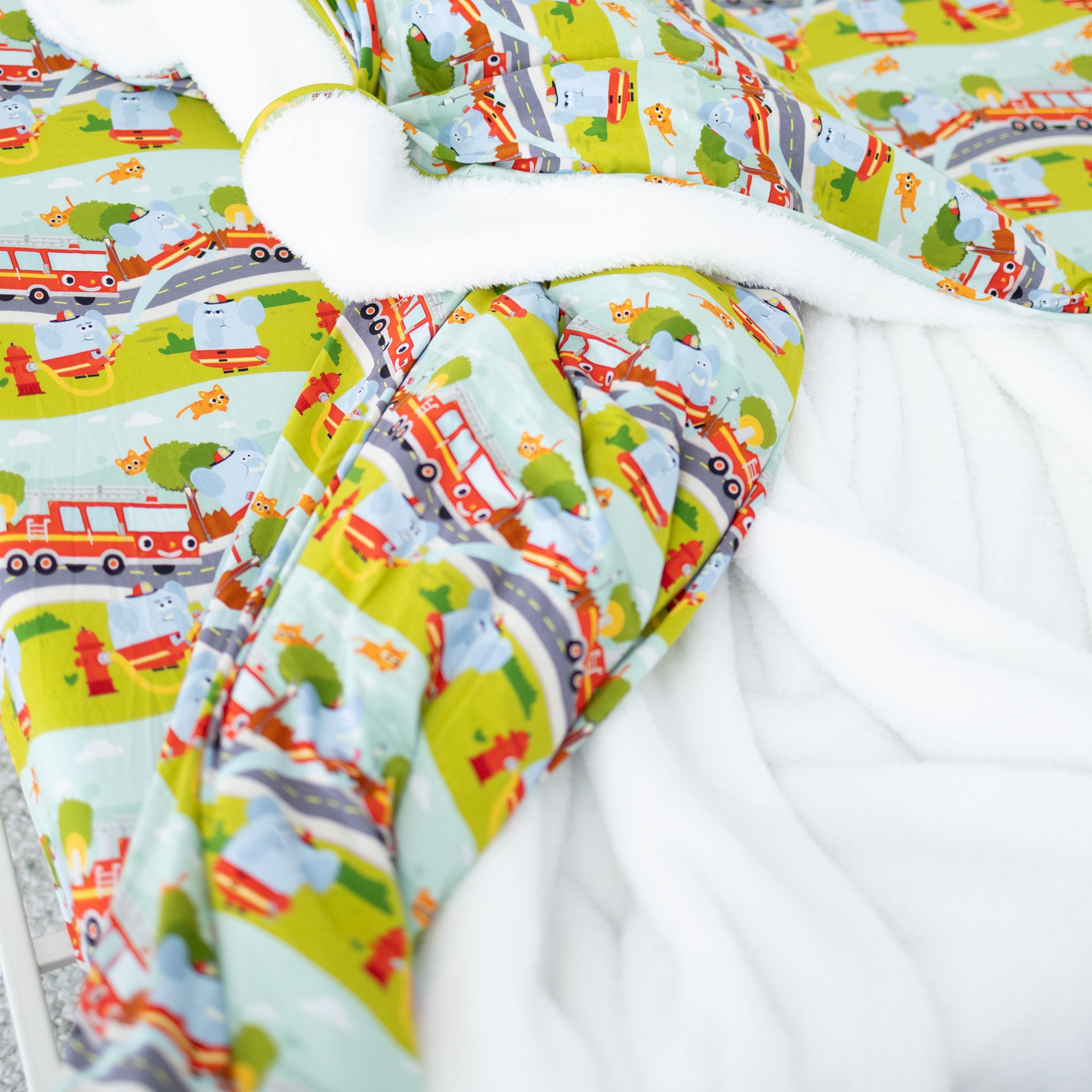 A plush blanket featuring a colorful firetruck and elephant pattern with a soft white underside.