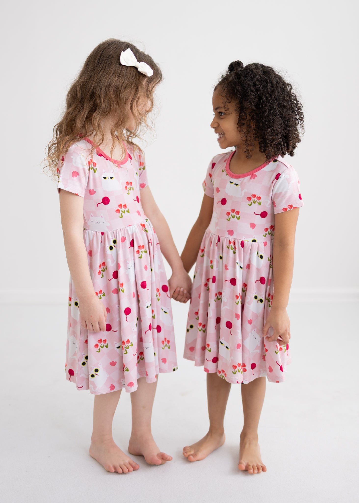 Two girls hold hands wearing pink dresses with a cat and tulip pattern.