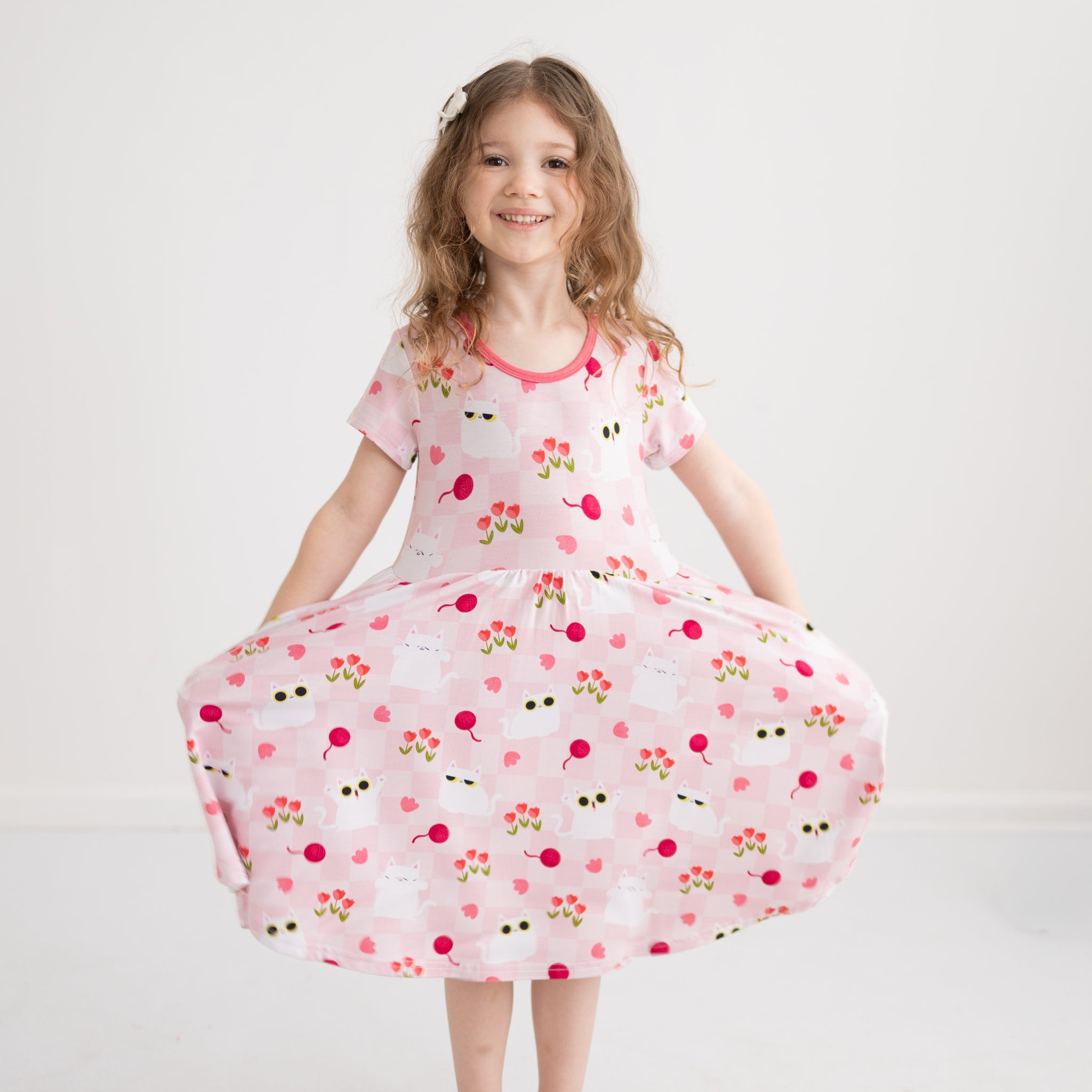 A girl wears a pink and white checkered dress featuring a cat and tulip print.