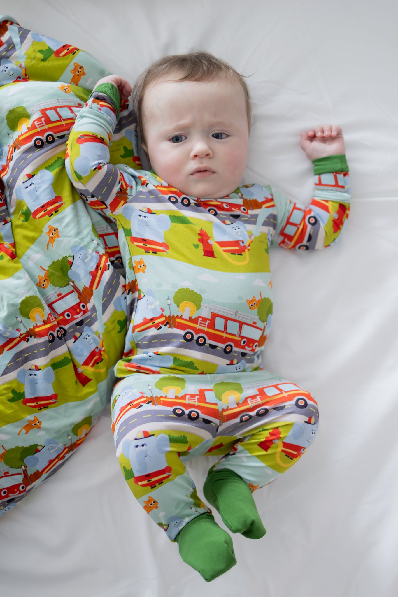 A baby wearing a long-sleeve pajama set featuring a colorful firetruck and elephant print.