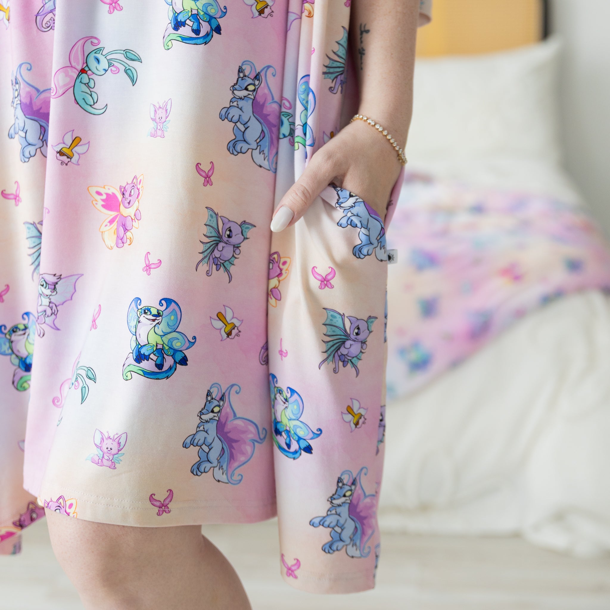 A person wears a pink Neopets Faerie print sleep tee featuring a side pocket.