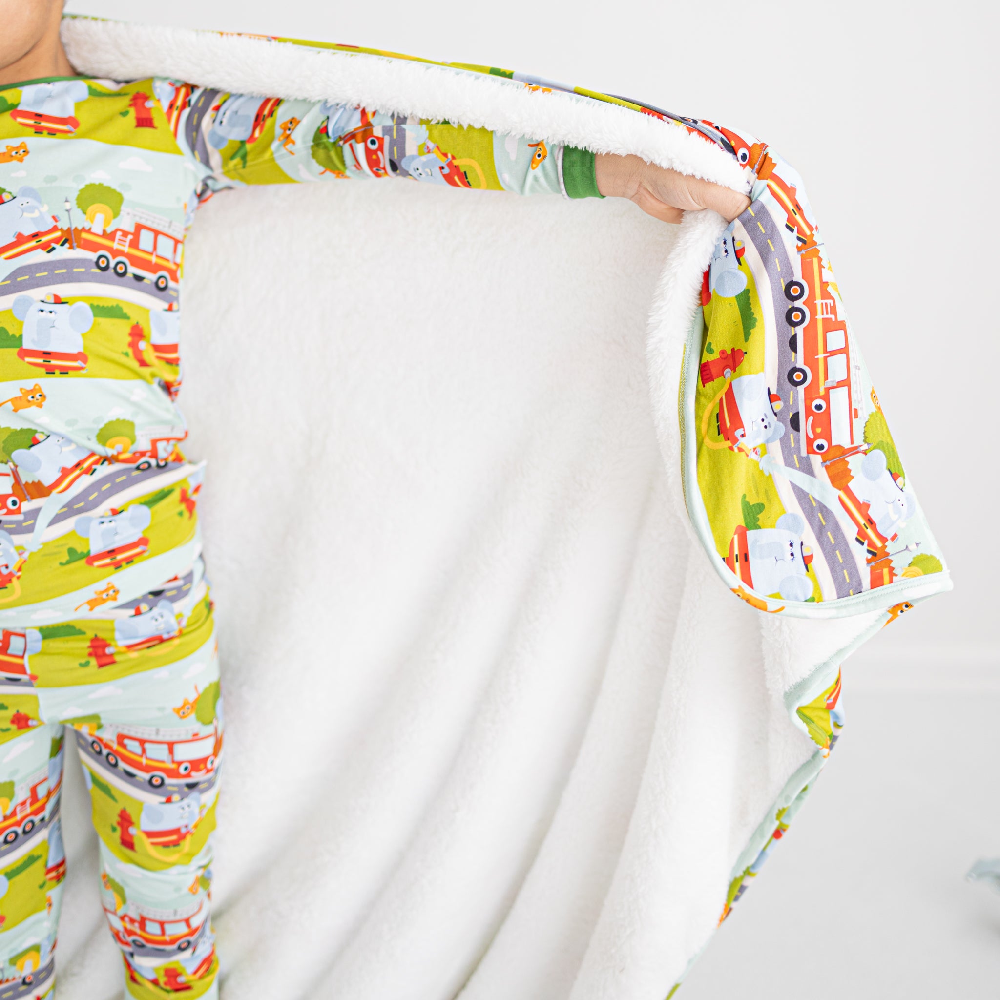 A child wears matching pajamas and holds a plush blanket featuring a firetruck pattern.