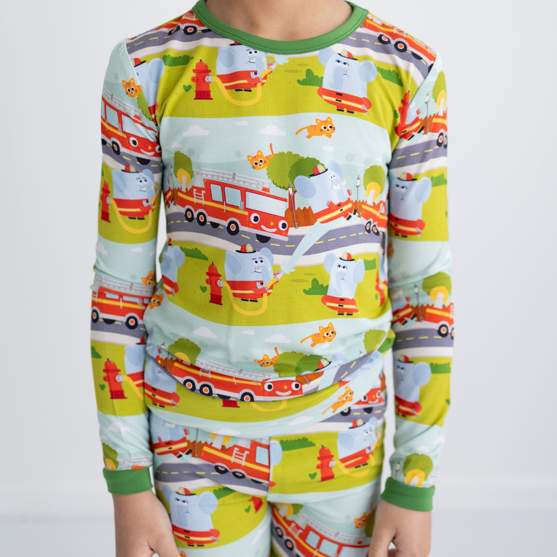 A child wears a long-sleeve pajama set featuring a colorful firetruck and elephant print.
