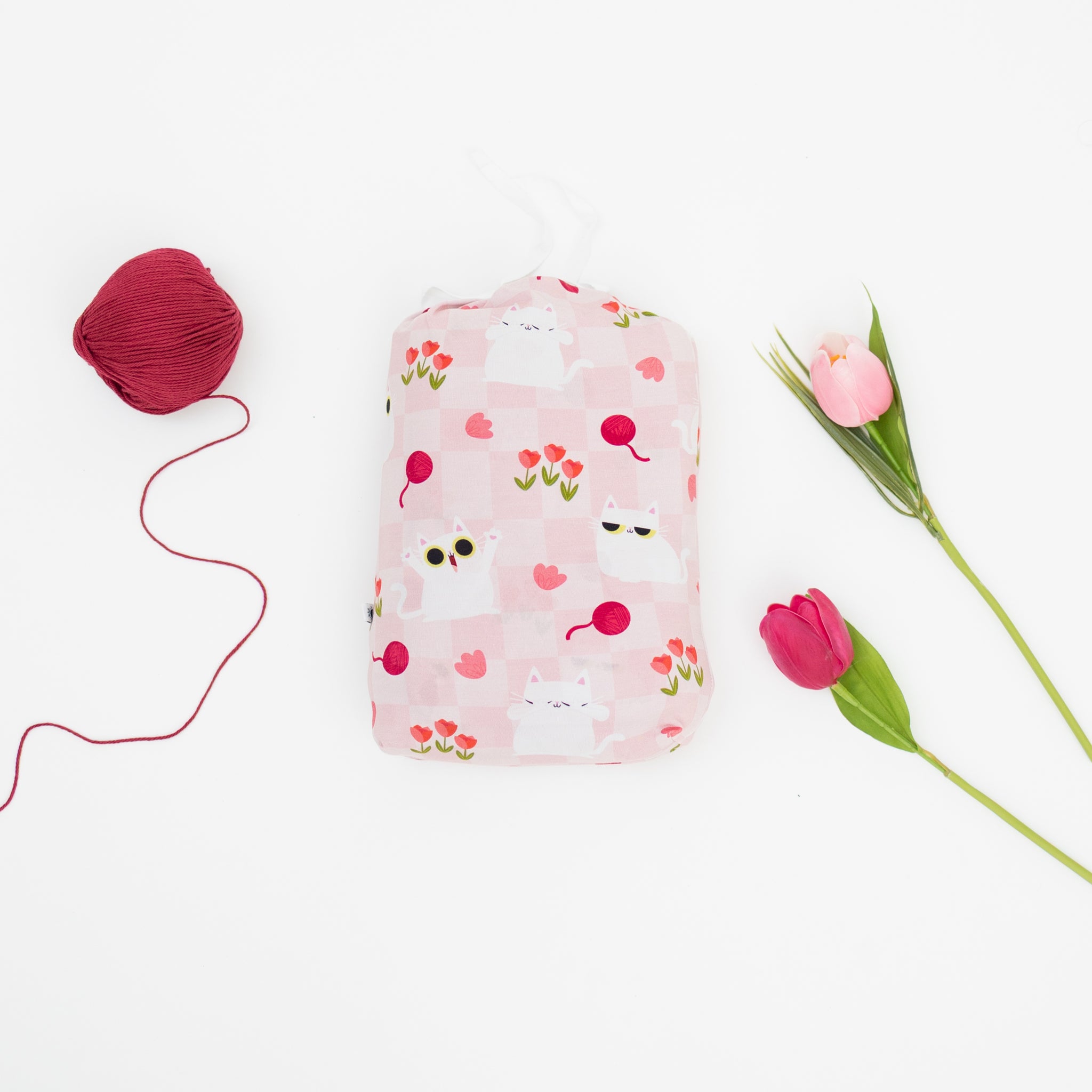 A pink twin sheet and pillowcase set featuring a cat and tulip pattern, shown with yarn and flowers.