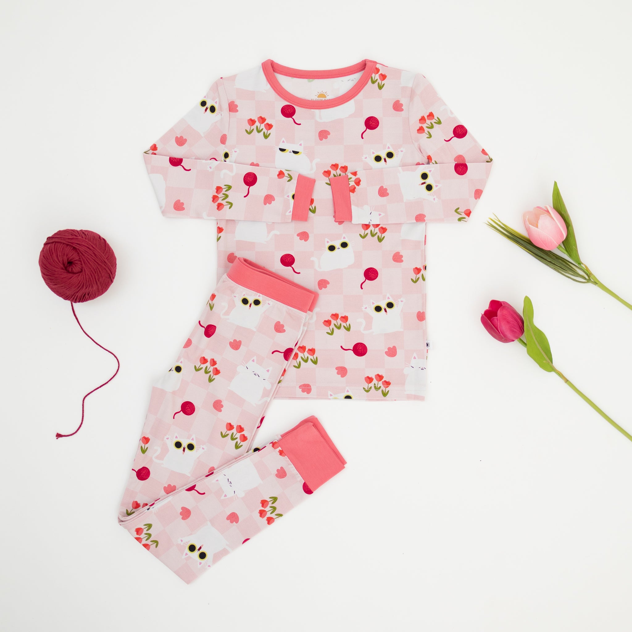 A pink and white checkered pajama set featuring a cat and tulip print with a ball of yarn.