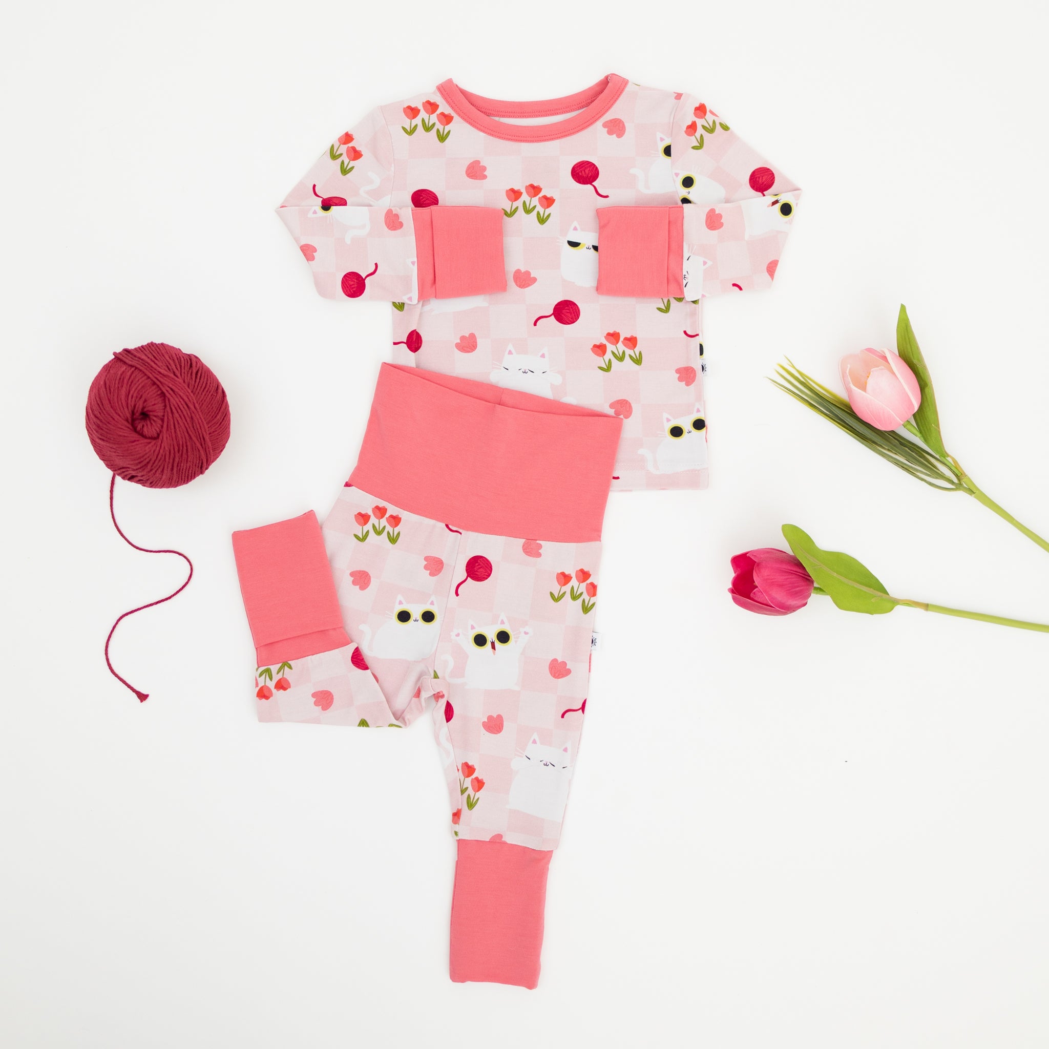 A pink and white checkered pajama set featuring a cat and tulip print with solid pink cuffs.
