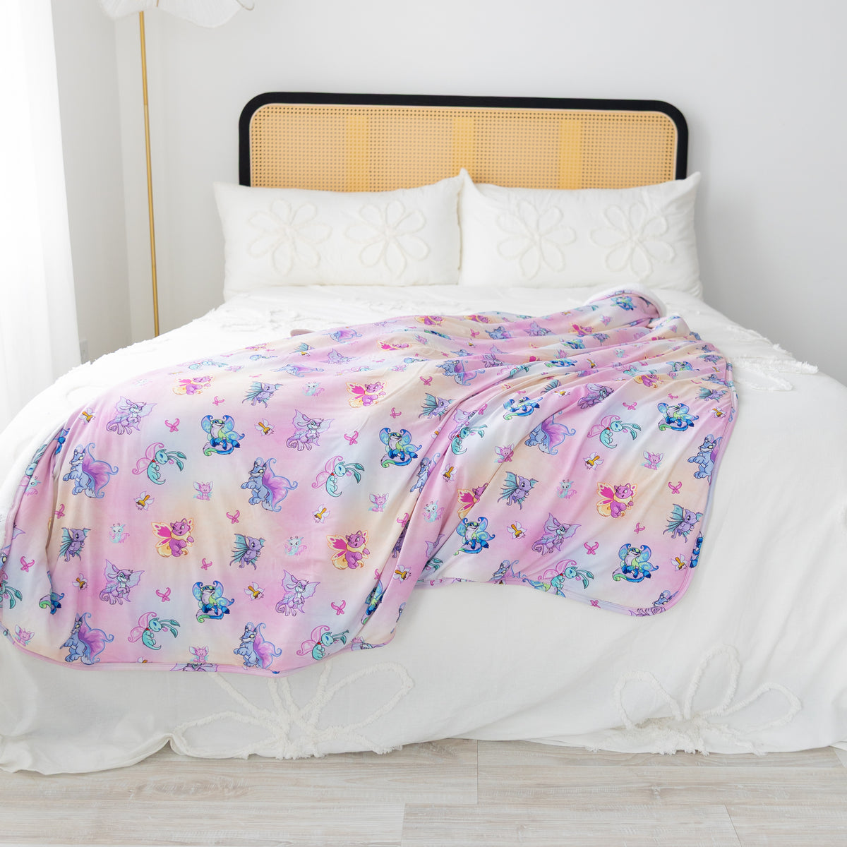 A soft pink and purple Neopets Faerie patterned plush blanket draped over a white bed.