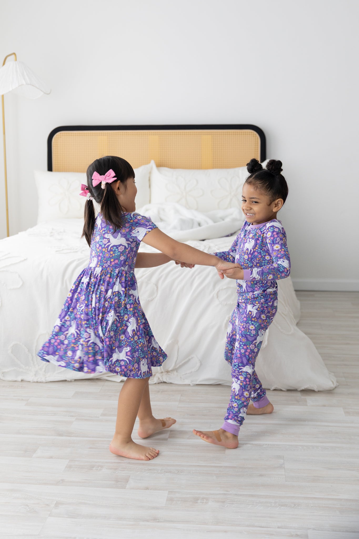 Two girls hold hands while wearing matching purple unicorn-print Tencel Modal pajamas.