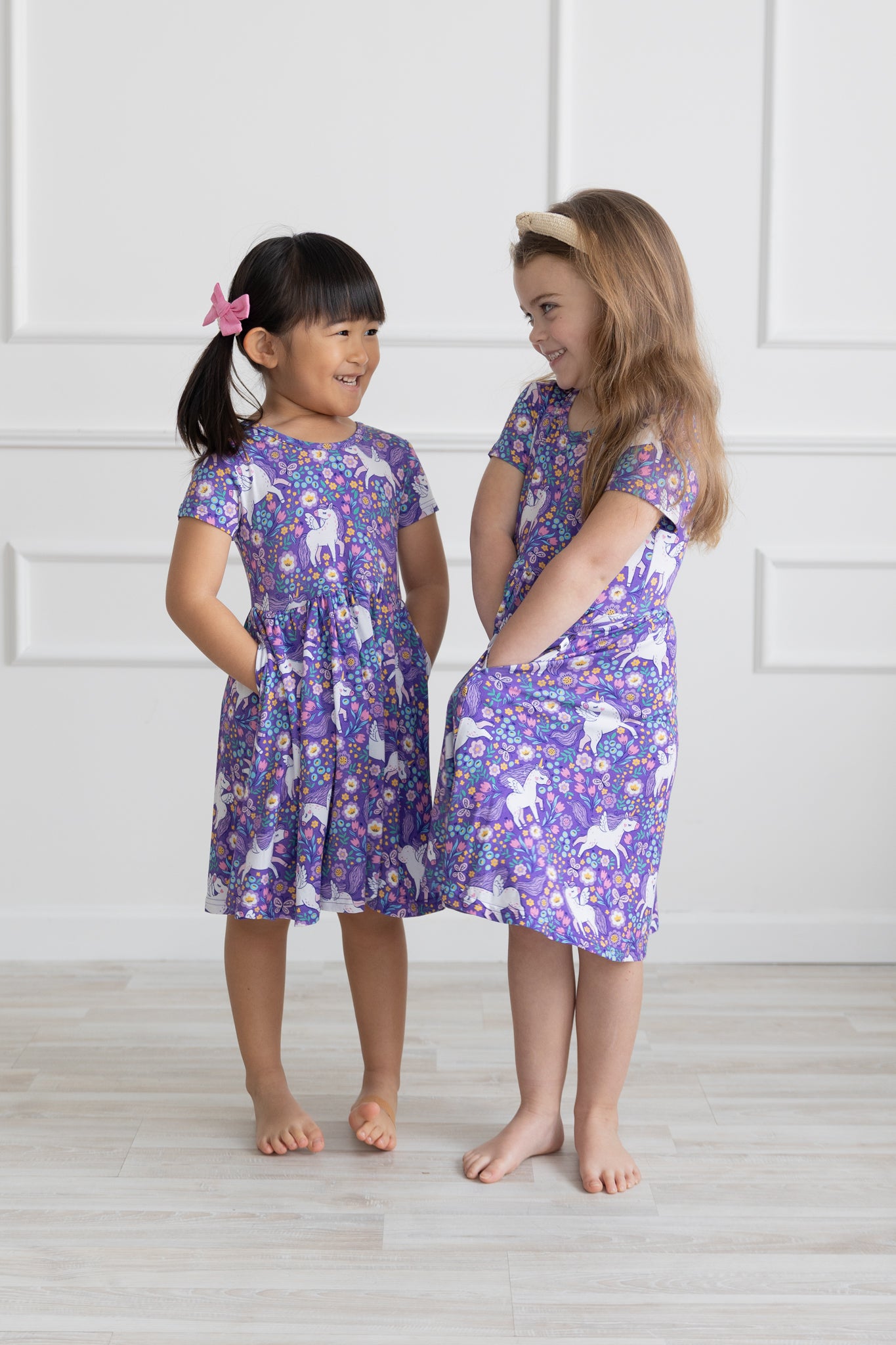 Two girls wearing purple short-sleeve dresses with a unicorn and floral print.